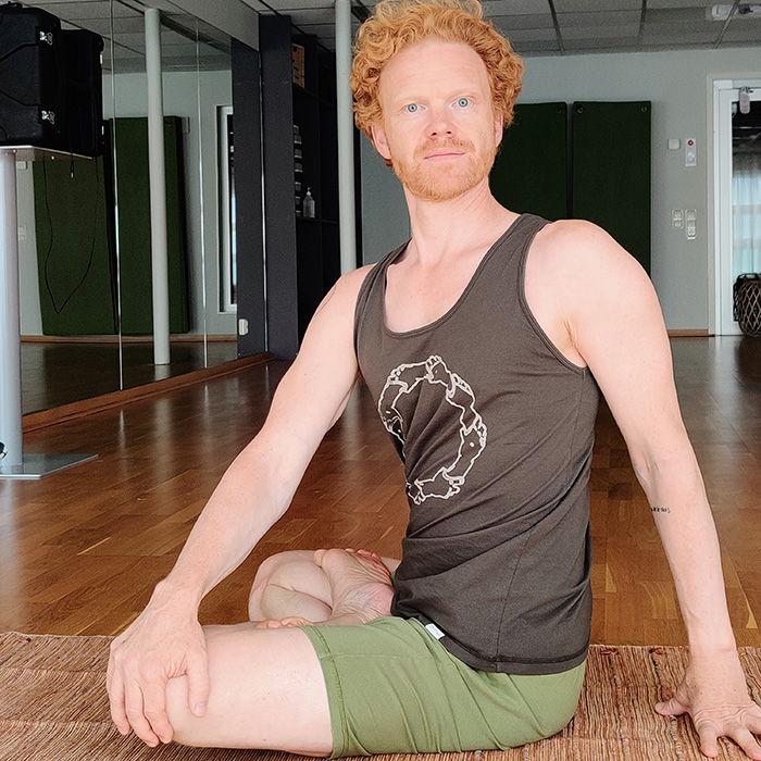 Stefan En man som siter med korslagda ben på en yogamatta och tittar in i kameran